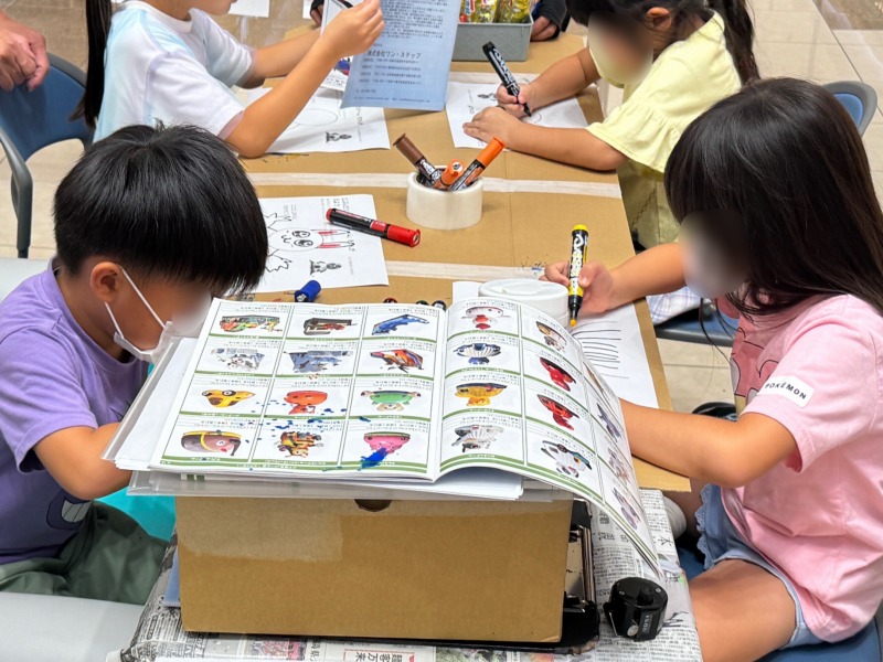 遊具カタログを見ながらドーム型遊具のイラストを描くお子様